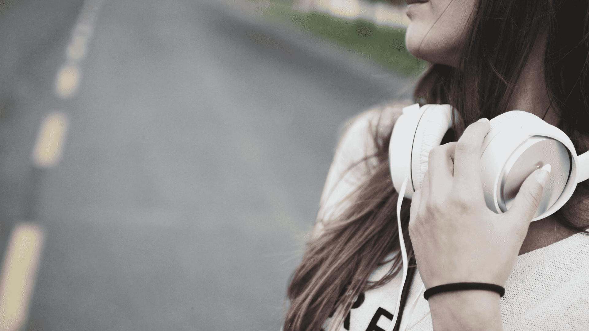 Kvinna med hörlurar i handen, stående på en väg, redo att lyssna på en podcast._